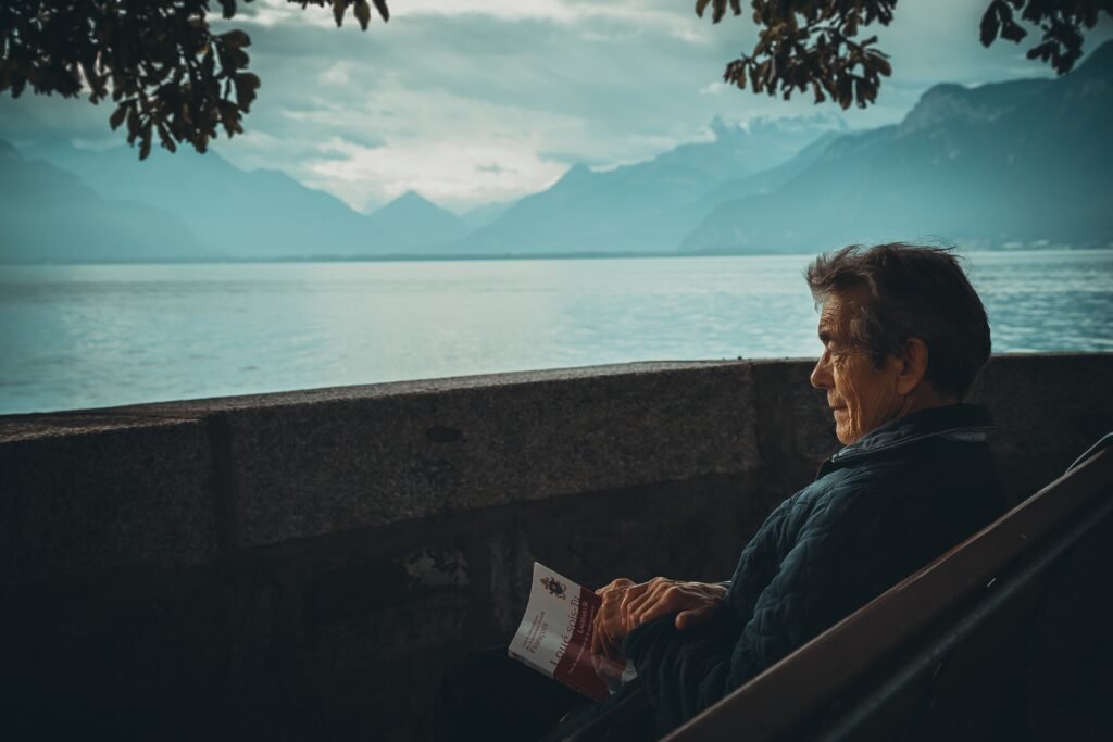 man-sitting-while-holding-a-book-watching-on-body-of-water